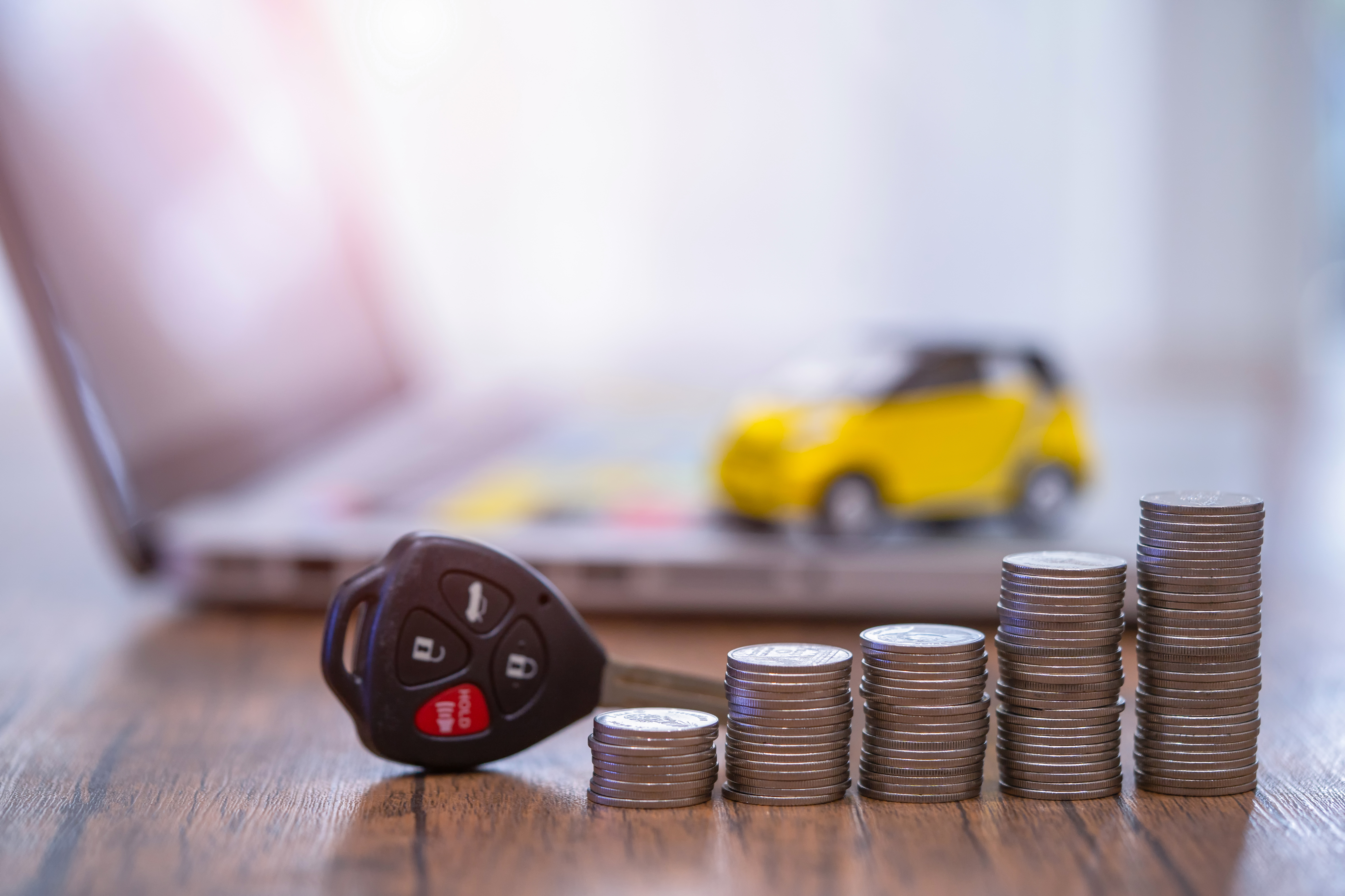 A car key and ascending stacks of coins in front of an open laptop