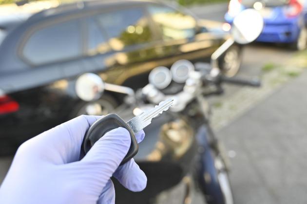 A glove-protected hand holds motorcycle key in front of motorcycle